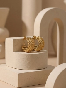 Detail shot of C-shaped crisscross textured gold earrings on a minimalist stone display
