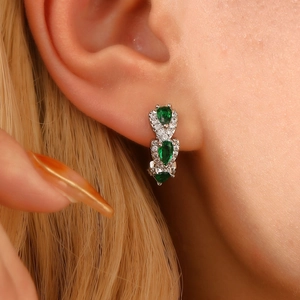 Close-up of emerald drop earrings featuring triple teardrop stones and pavé halo setting