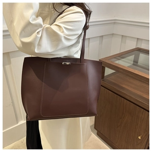 Detail of a large brown faux leather tote bag worn by a model in a minimalist setting