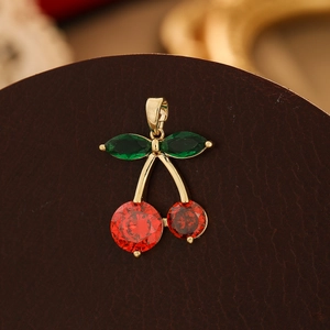 Macro shot of cherry pendant with red cubic zirconia and green marquise leaves on leather