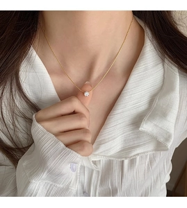 Detail of a gold zircon pendant necklace worn by a model on a white pleated shirt