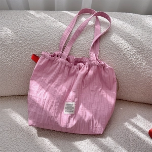 Detail of pink pleated tote bag with drawstring texture and brand label on soft background