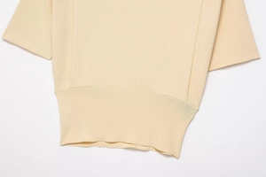 Detail of the fine knit texture and ribbed hem on this cream short-sleeve top