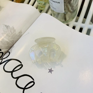 Detailed close-up of a pearlescent acetate hair claw clip with metallic spring on a book