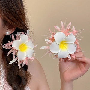 Close-up detail of plumeria fabric flower hair clip with pink accents worn by model