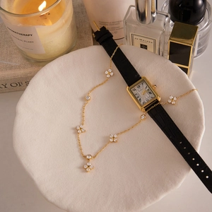 Detail view of gold clover necklace with stones and rectangular watch on ceramic tray