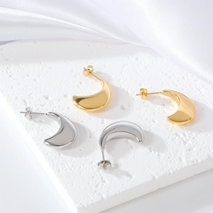 Macro detail of minimalist gold and silver crescent stud earrings on a stone base