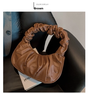 Detail of a brown pleated crescent bag with cloud-like texture on a leather chair