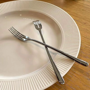 Modern stainless steel fruit fork and spoon set displayed on a white ceramic plate