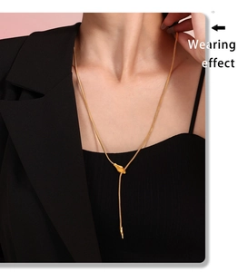 Close-up of gold snake chain lariat necklace with leaf pendant on model wearing black suit