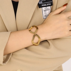Close-up of a minimalist geometric gold titanium bracelet worn by a model in a beige suit