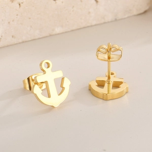 Detailed close-up of golden anchor-shaped stud earrings on a textured stone base