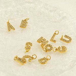 Close-up of gold-plated letter pendants with shiny zircon stones on a glass surface