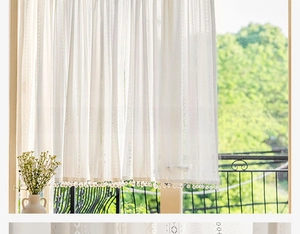 Detail of white sheer cafe curtain featuring hollow stripes and decorative pom-pom fringe