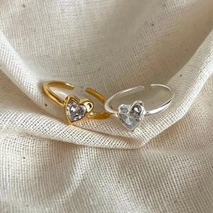 Detailed view of silver and gold heart-shaped zircon rings on soft linen fabric
