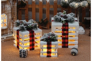 Close-up of three lighted wooden Christmas gift boxes with snow, pine cones and red berries