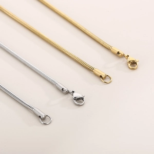 Detail view of gold and silver snake bone necklaces with lobster clasps on a beige background