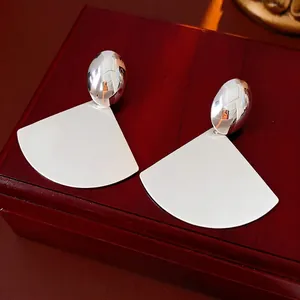 Minimalist silver steel fan earrings with brushed matte finish on a dark wooden box