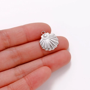 Macro detail of a shell-shaped stainless steel pendant held on a fingertip for size scale