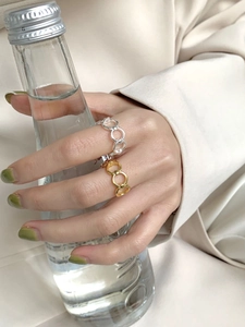 Close-up of minimalist gold and silver chain link rings worn by a model holding a glass