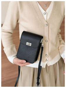 Detail of black cross-grain leather phone bag with silver twist lock on beige cardigan