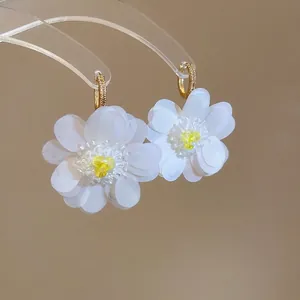 Elegant zircon flower pendant earrings with white petals and gold hoops on a display stand