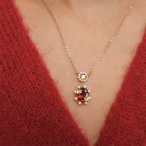 Detail of 18K gold plated necklace with oval red gemstone and orange zircon charms