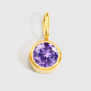 Detail of round golden pendant featuring a faceted purple birthstone on white background