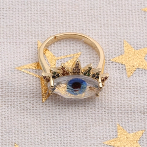 Macro detail of golden Evil Eye ring with colorful zircons on a star pattern background