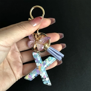 Close-up of letter X resin keychain with purple tassel and gold butterfly charm