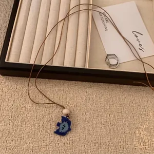 Detail der blauen Cartoon-Smiley-Halskette mit weißen Perlen auf gewebtem Hintergrund