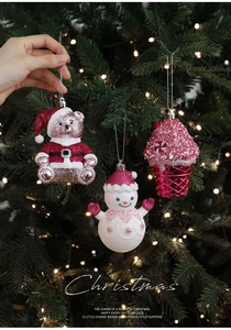 Detail of red bear and pink snowman glitter ornaments hanging on a Christmas tree