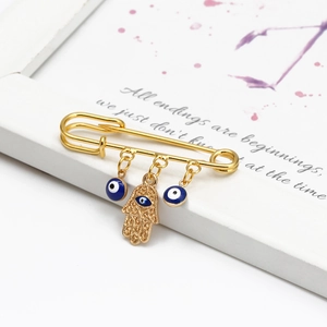 Detail of a golden safety pin brooch with blue evil eye beads and a Hamsa hand charm