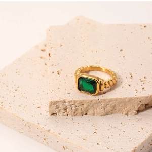 Detailed view of an emerald-cut green stone ring with gold twisted band on stone pedestal