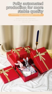 Deep red gift box with gold ribbon featuring plush bunny toy and decorative foam balls