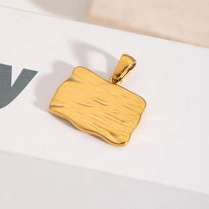 Détail d'un pendentif rectangulaire en acier doré avec une texture ondulée irrégulière