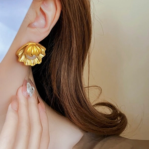 Close-up of vintage golden shell earrings with pearl detail worn by a model in soft light