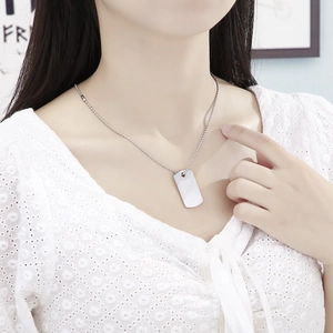 Close-up of a silver polished rectangular dog tag pendant on a bead chain worn by a model