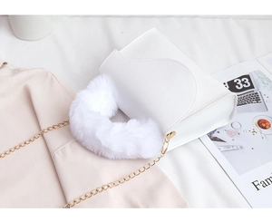 Close-up of white crossbody bag featuring soft faux fur handle and gold chain strap