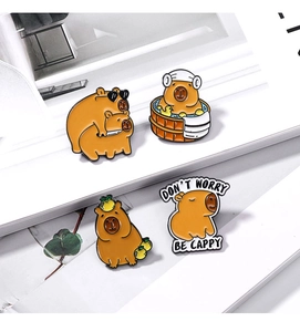 Détail de quatre épingles en émail Capybara créatives avec texte motivant sur un livre