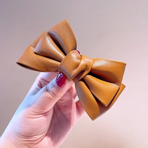 Détail du nœud papillon en cuir marron caramel montrant la texture et les coutures