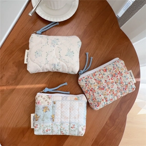 Flat lay of three floral quilted cotton pouches with zippers on a wooden table