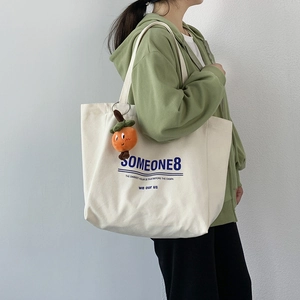 Minimalist off-white large canvas tote bag with letter print and fruit pendant on model