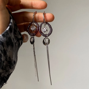 Detailed shot of long silver tassel earrings with purple acrylic rings and zircon accents