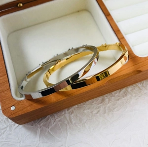 Gold and silver stainless steel X-bracelets with rivet details in a wooden jewelry box