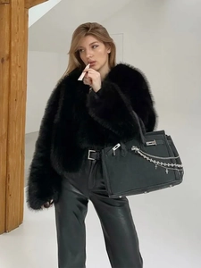 Detail of black faux fur coat styled with a leather bag and metal chain accessories