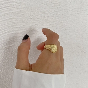 Detail of gold irregular lava textured ring worn on hand against a white background