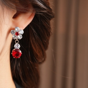 Macro shot of zircon flower earrings with red and clear crystals on model's ear
