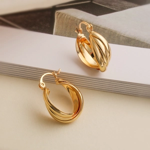 Detailed view of twisted gold-plated hoop earrings on a soft beige background