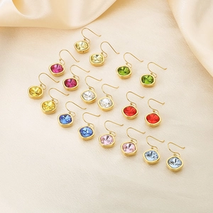 Macro shot of 18k gold plated earrings with colorful square-cut zirconia on silk fabric